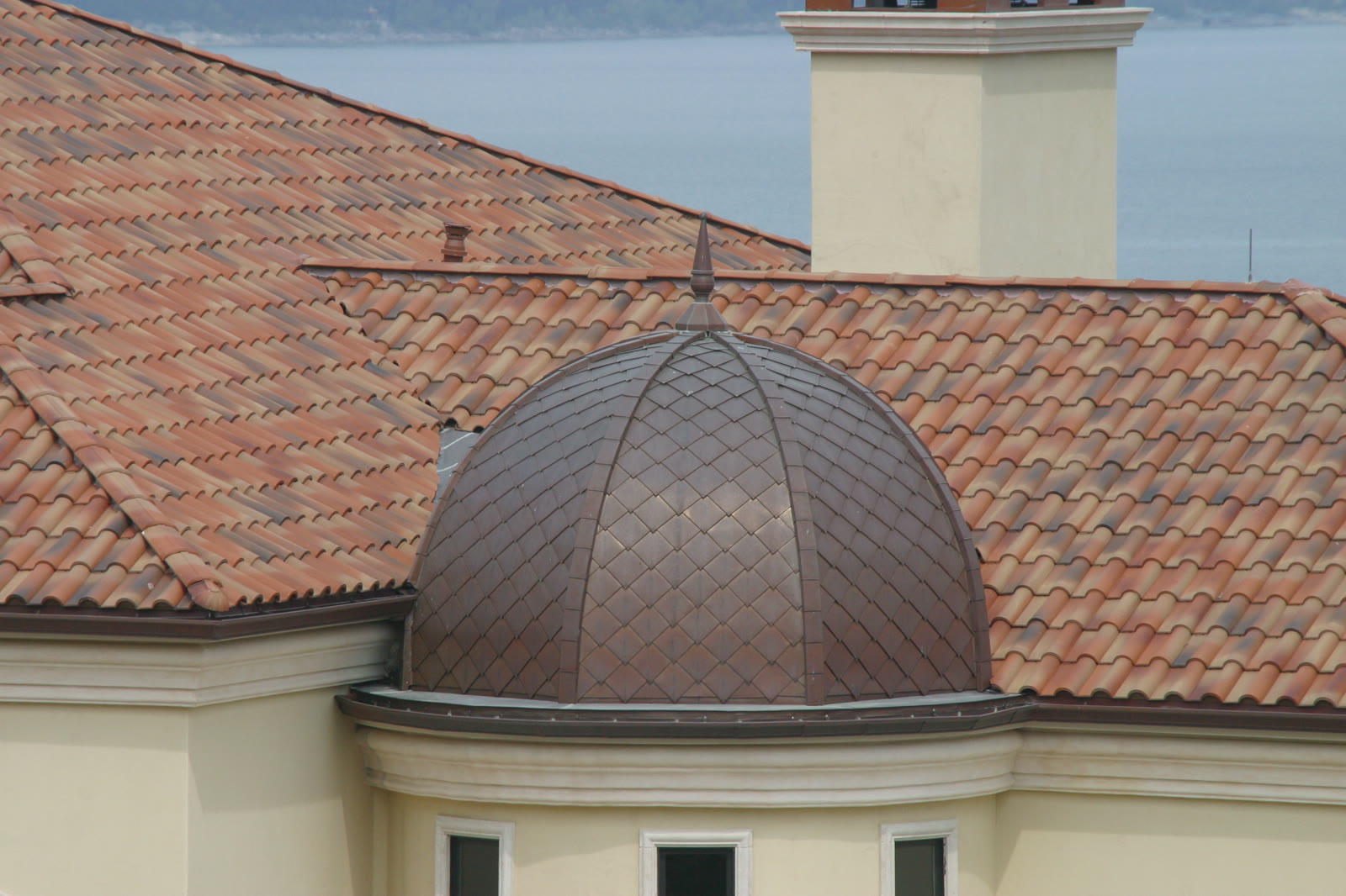 Copper dome rising from a clay tile roof field, with twin chimney pots