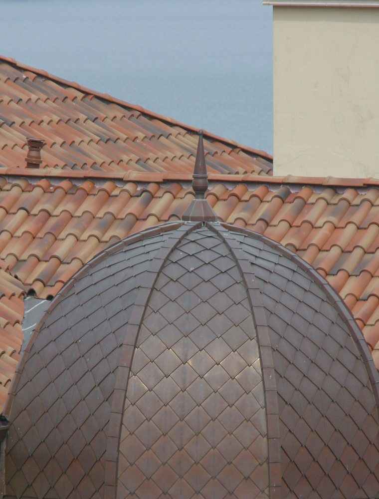 Copper scale-tiled dome with a cast finial, set into a clay-tile roof